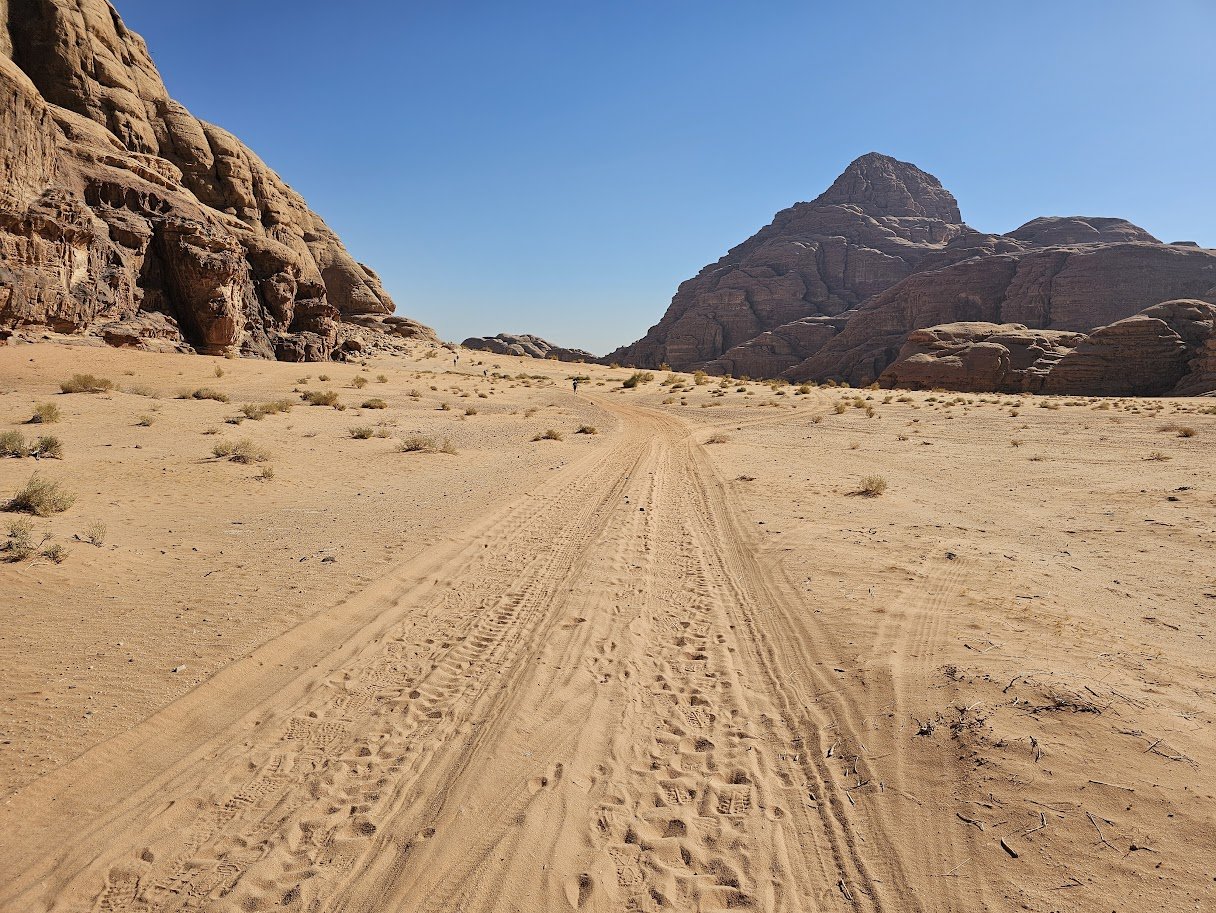 Vehicle tracks leading through the desert sand of Wadi Rum, Jordan, with rock formations rising on either side